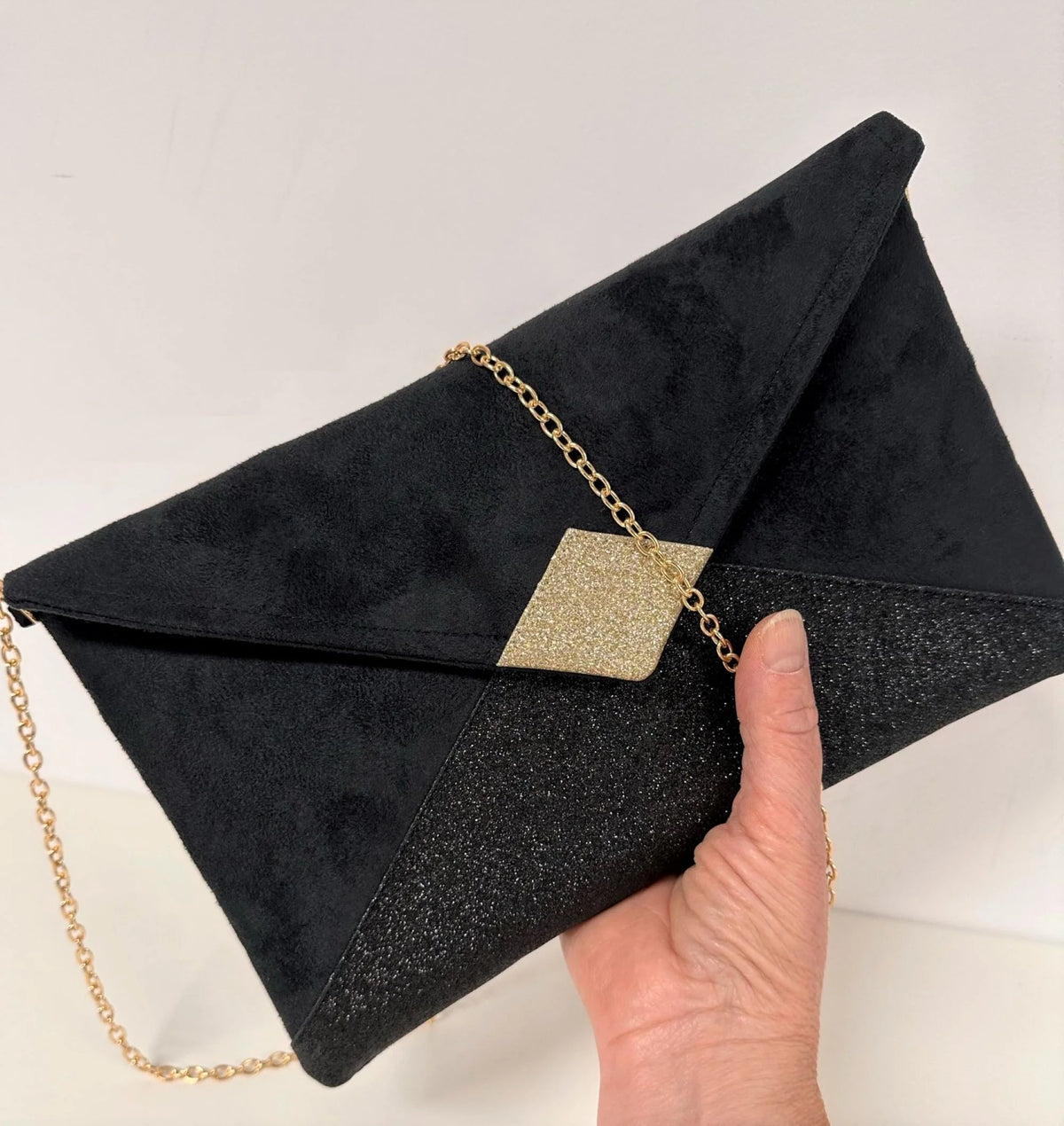 Le sac pochette Isa noir et doré à paillettes, tenu en main.