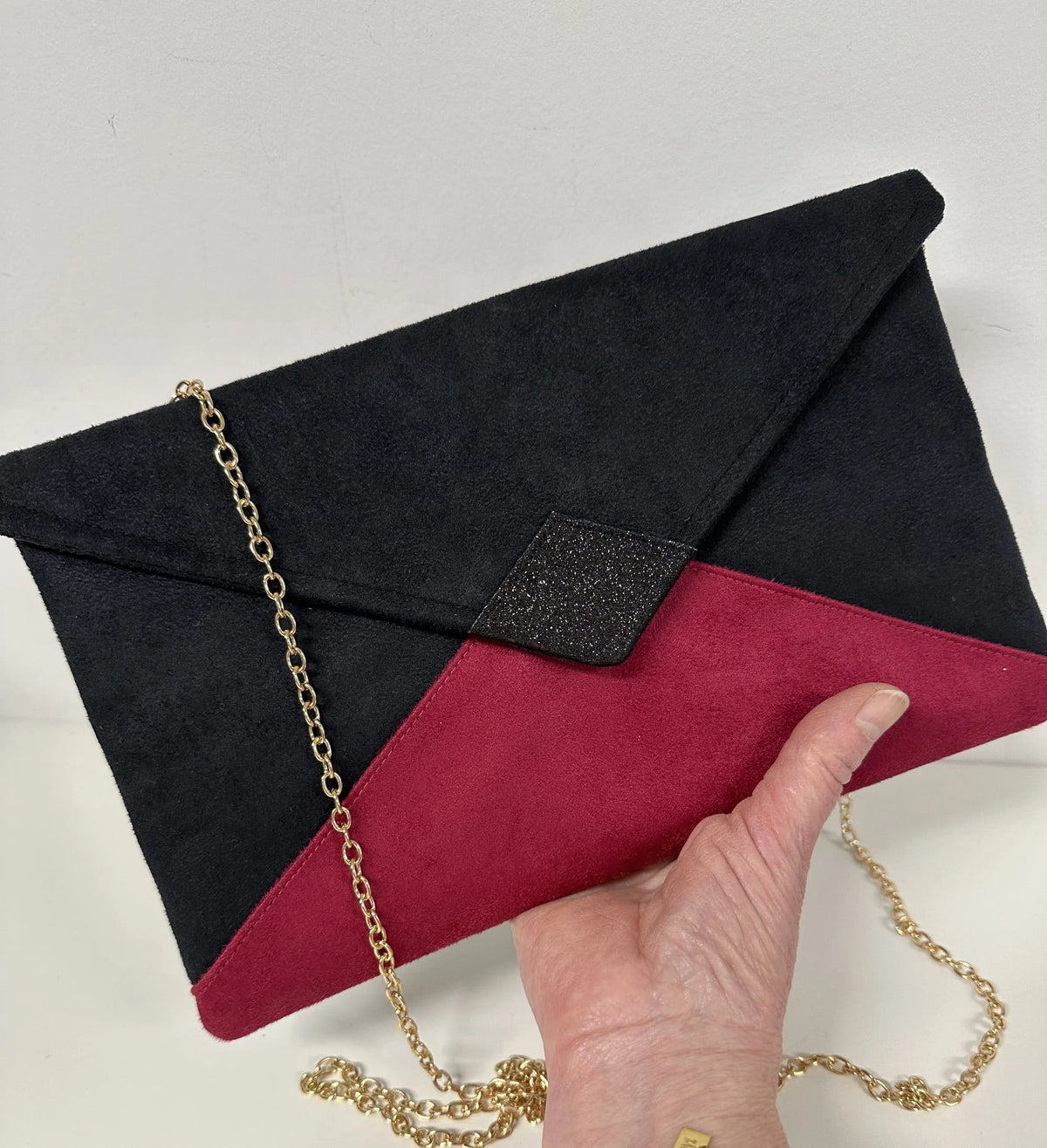 Le sac pochette Isa noir et fuchsia à paillettes  porté à la main.