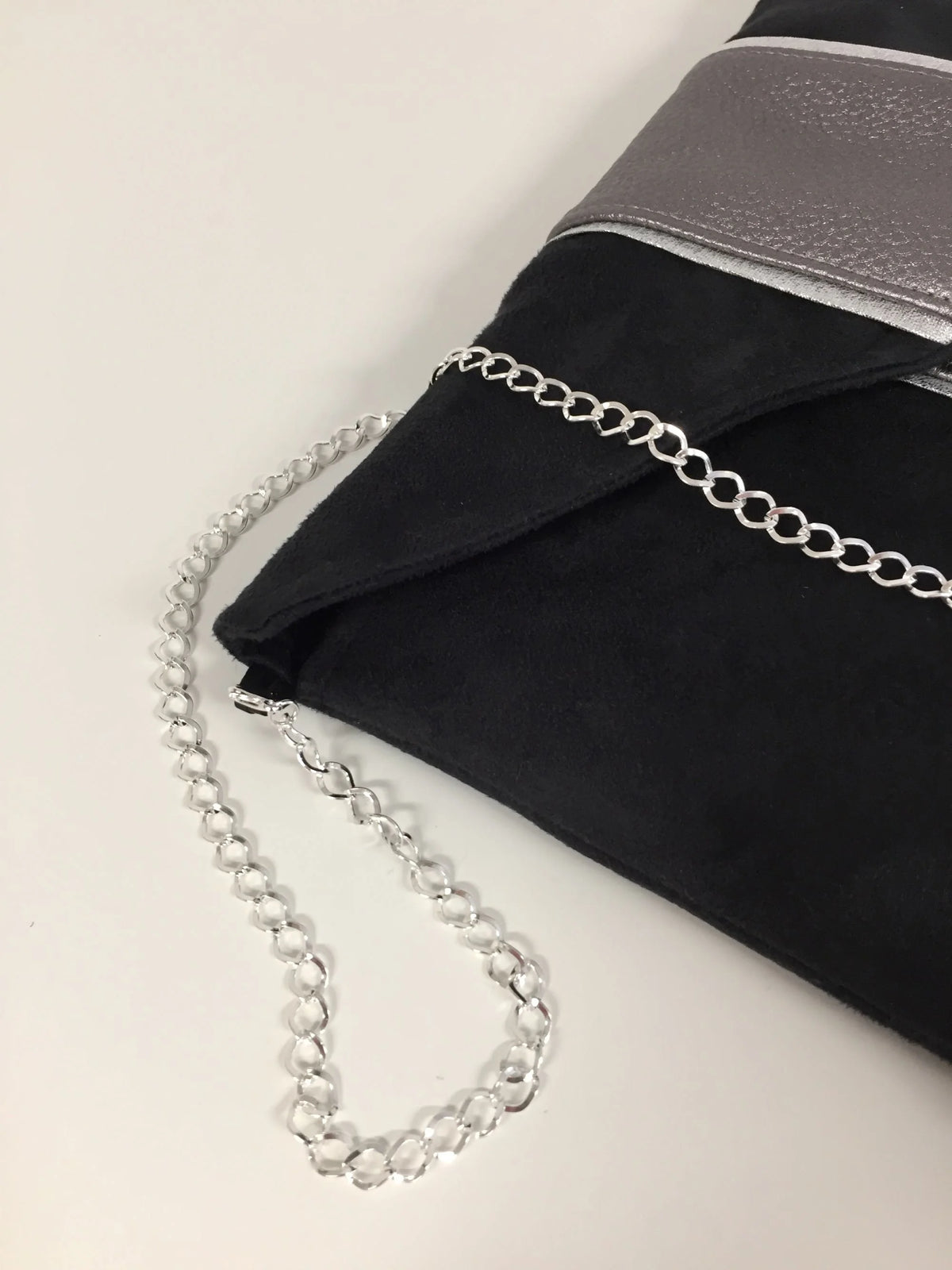 La chainette amovible du  sac pochette Isa noir et gris irisé à liseré argenté.