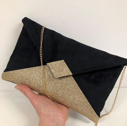 Le sac pochette Isa noir à paillettes dorées, avec chainette amovible, tenu en main.