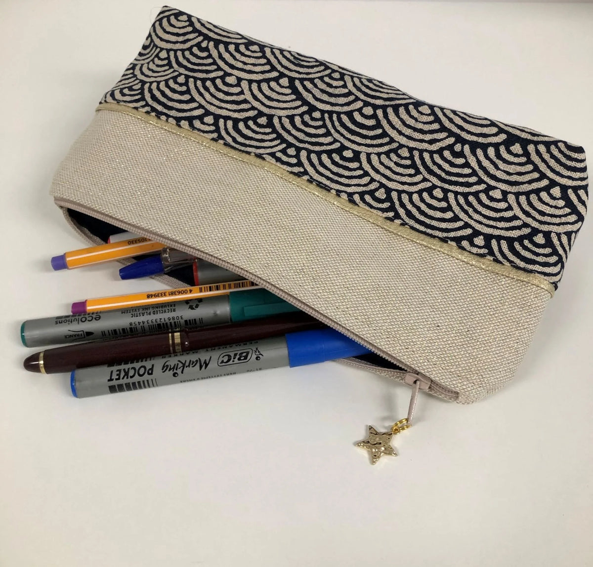 La trousse à stylos en tissu japonais bleu nuit et doré, contenant plein de crayons.